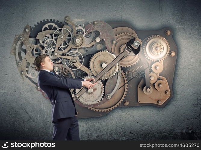 Working mechanism. Young businessman fixing gears mechanism with wrench