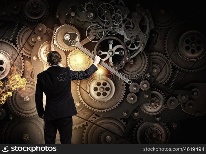 Working mechanism. Young businessman fixing gears mechanism with wrench