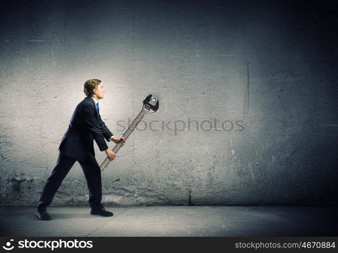 Working mechanism. Young businessman fixing gears mechanism with wrench