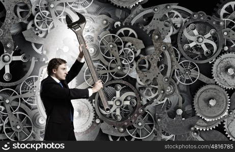 Working mechanism. Young businessman fixing gears mechanism with wrench