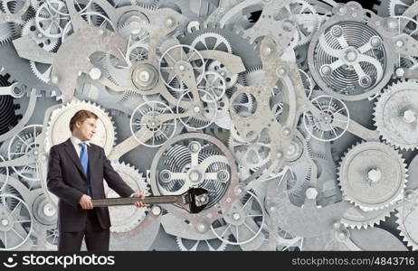 Working mechanism. Young businessman fixing gears mechanism with wrench