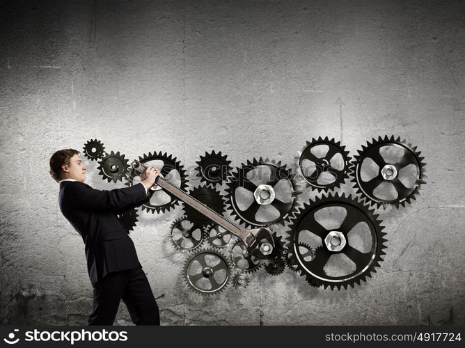 Working mechanism. Young businessman fixing gears mechanism with wrench