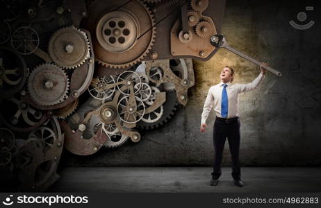 Working mechanism. Young businessman fixing gears mechanism with wrench