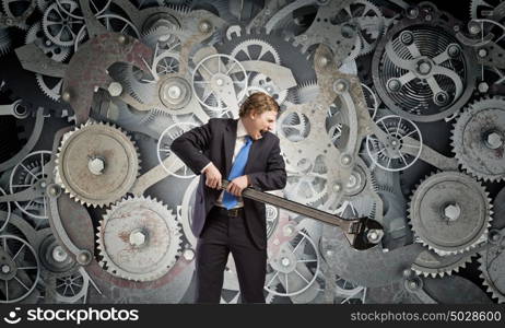 Working mechanism. Young businessman fixing gears mechanism with wrench