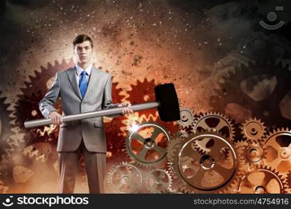 Working mechanism. Young businessman with hammer against gears background