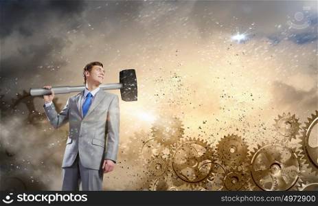 Working mechanism. Young businessman with hammer against gears background