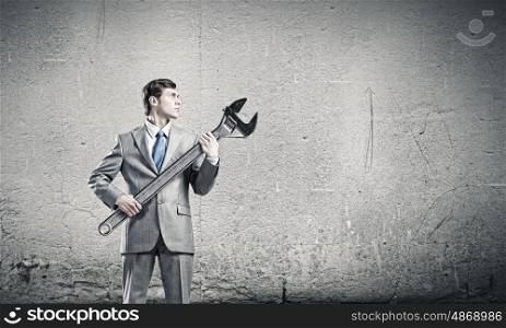 Working mechanism. Young businessman with wrench against cement background