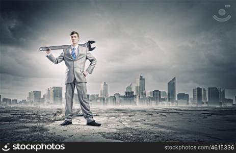 Working mechanism. Young businessman with wrench against city background