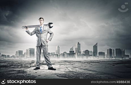 Working mechanism. Young businessman with wrench against city background