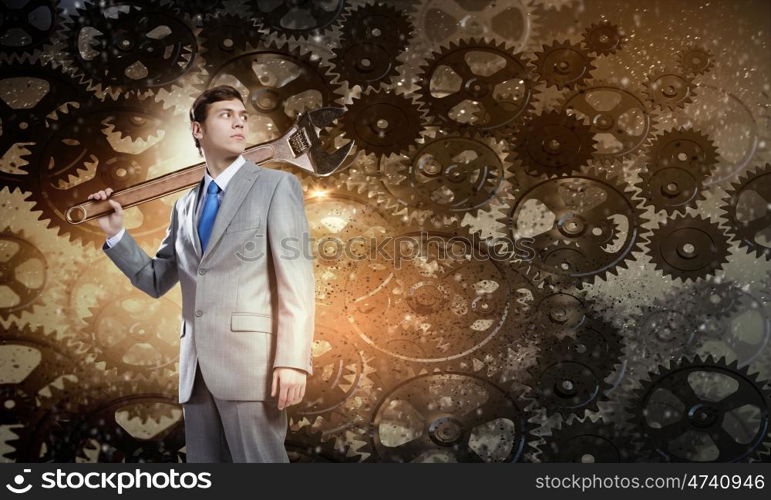 Working mechanism. Young businessman with wrench against mechanism background