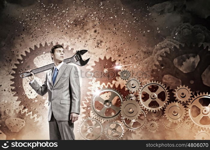 Working mechanism. Young businessman with wrench against mechanism background