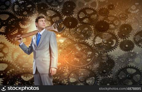 Working mechanism. Young businessman with wrench against mechanism background
