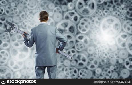 Working mechanism. Young businessman with wrench against mechanism background