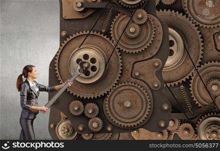 Working mechanism. Young businesswoman fixing gears mechanism with wrench