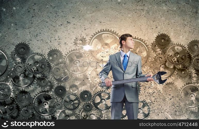 Working mechanism. Young determined businessman with wrench in hands and cogwheels at background