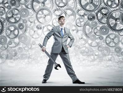 Working mechanism. Young determined businessman with wrench in hands and cogwheels at background