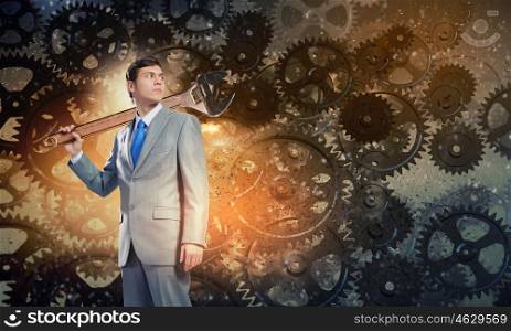 Working mechanism. Young determined businessman with wrench on shoulder and cogwheels at background
