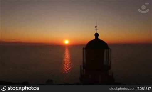 Working old lighthouse on a sunset background in the sea in summer. Aerial flying of the drone past the lighthouse at sunset. Lighthouse gives light signals to ships in the sea