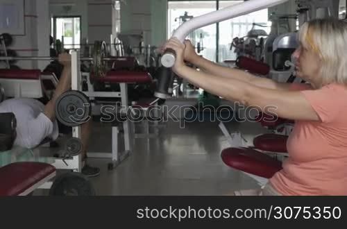 Working out in the gym. Senior woman exercising on chest press machine and senior man doing bench press