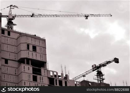 Working tall cranes inside place for with tall buildings under construction against a clear blue sky. Crane and building working progress. Retro tone