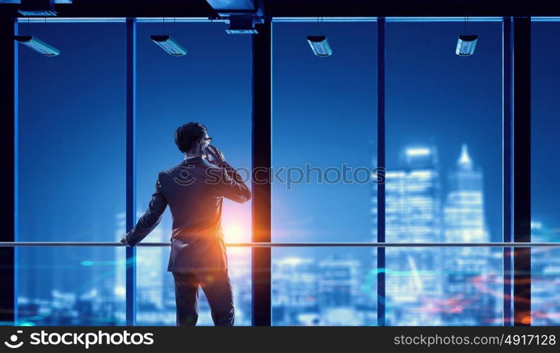 Working till late night. Young businessman with mobile phone against night city background