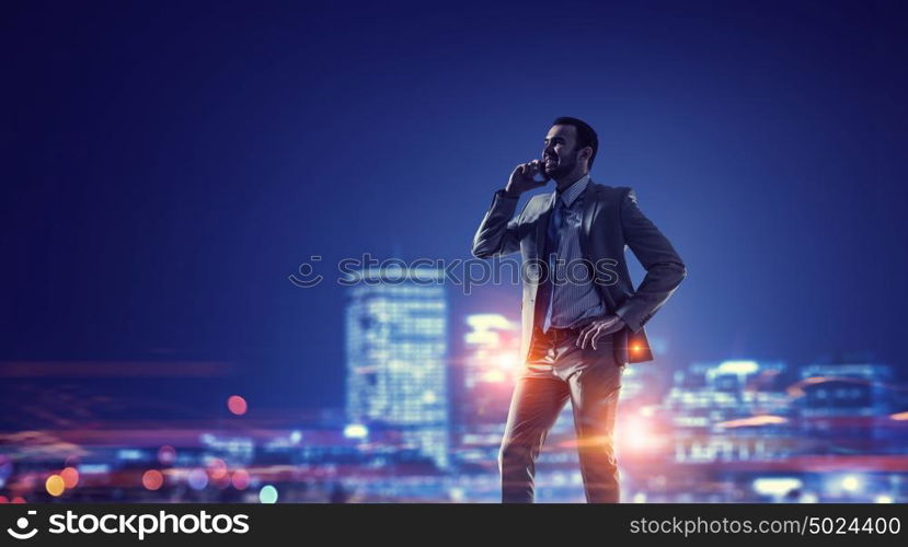 Working till late night. Young businessman with mobile phone against night city background