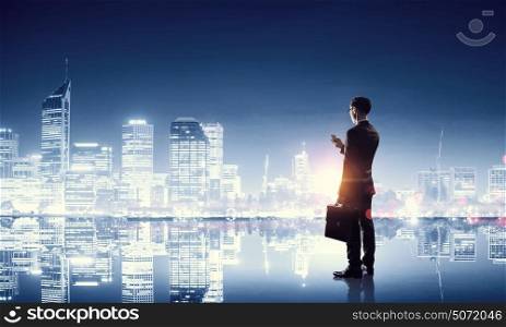 Working till late night. Young businessman with mobile phone against night city background