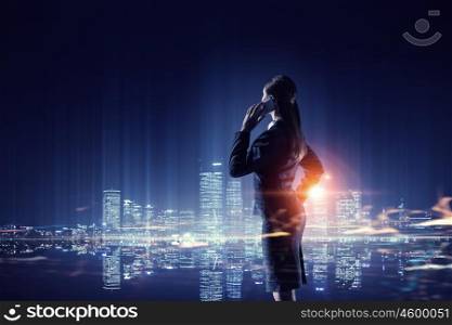 Working till late night. Young businesswoman with mobile phone against night city background