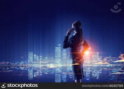 Working till late night. Young businesswoman with mobile phone against night city background