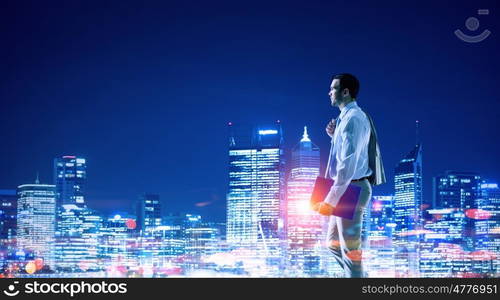 Working till late night. Young elegant businessman against night city background