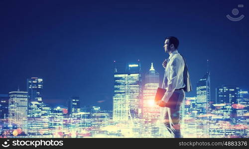 Working till late night. Young elegant businessman against night city background