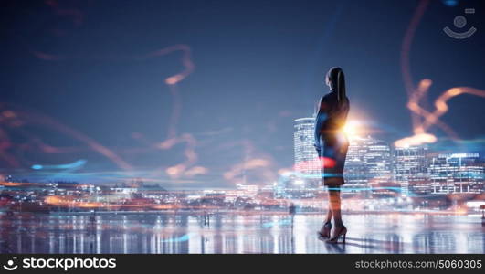 Working till late night. Young elegant businesswoman against night city background