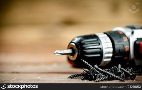 Working tool. Screwdriver with self-tapping screws on the table. On a wooden background. High quality photo. Working tool. Screwdriver with self-tapping screws on the table.