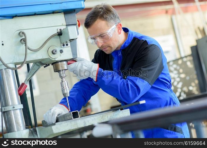 Workman drilling through square steel bar