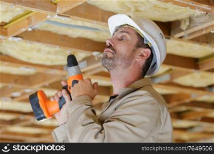 workman holding cordless drill looking up at roof timbers