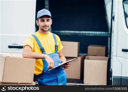 Workman or courier in uniform holds carton box in hands, truck with parcels on background. Distribution business. Cargo delivery. Empty, clear container. Workman or courier holds carton box in hands
