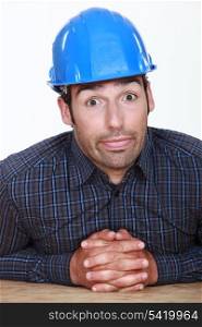workman sitting at table with joined hands making grimace