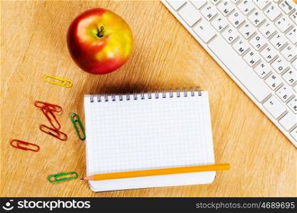 Workplace. Red apple notepad and keyboard on wooden table