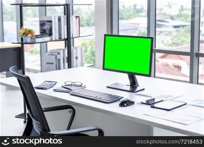 Workspace Business mockup desktop computer empty green screen with keyboard notebook and other accessories on Modern dark wooden office corner and black office chairs with window in office interior