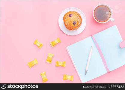 workspace desk styled design office supplies, hot tea, candy and cake on pink pastel background minimal style