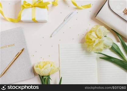 Workspace of a female blogger. Yellow flowers of spring tulips, notebooks with a pen, womens bag, gift with a yellow ribbon on a light background