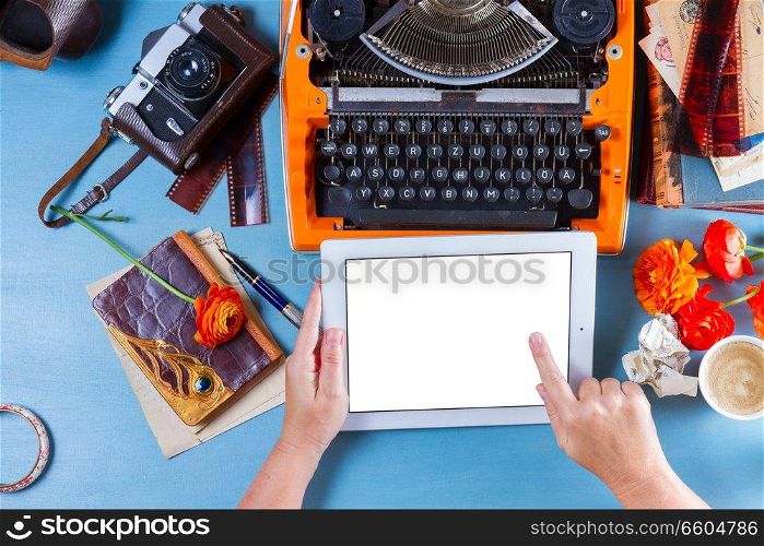 Workspace with orange retro typewriter, someone hands holding and pointinat modern tablet, copy space on screen. Workspace with vintage orange typewriter