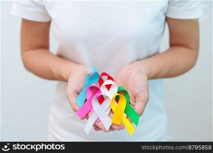 World cancer day, February 4. Hand holding blue, red, green, white, pink, grey and yellow ribbons for supporting people living and illness. Healthcare and Autism awareness day concept