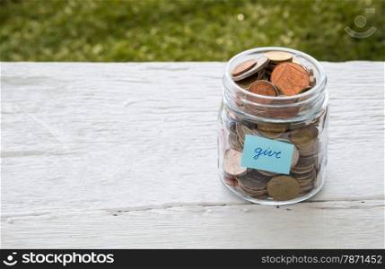World coins in money glass jar with blue GIVE word label place on white wood table, blank space for text, donation and charity concept