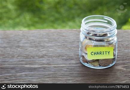 World coins in money glass jar with CHARITY word label place on natural wood table, blank space for text