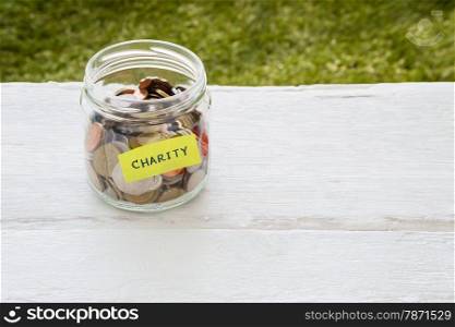 World coins in money glass jar with CHARITY word label place on white wood table, blank space for text