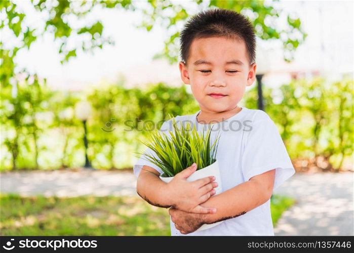 World Environment Day Environment and Save World Concept, Hand of Asian cute cheerful little child boy holding young tree on white pot on green garden background