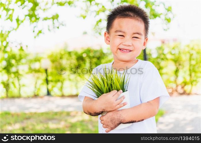 World Environment Day Environment and Save World Concept, Hand of Asian cute cheerful little child boy holding young tree on white pot on green garden background
