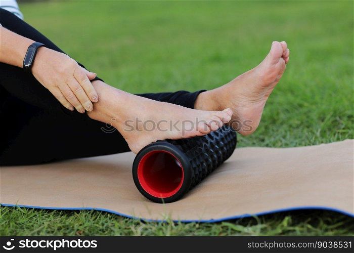 World health day. Unrecognizable woman warms up and works out the foot of the muscles of the body with a sport massage foam roller outdoors on green grass. Flexibility and mobility, body strength. World health day. Unrecognizable woman warms up and works out the foot of the muscles of the body with a sport massage foam roller outdoors on green grass. Flexibility and mobility, body strength.