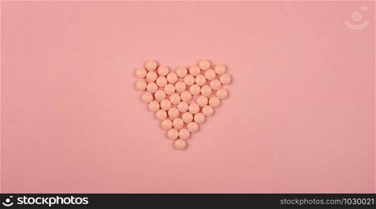 World Heart Day concept. Medical background. Pink Pills in form of heart on pink background. Flat lay. Heart health concept.